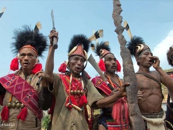 Group of tribal men dressed in traditional attire with weapons.