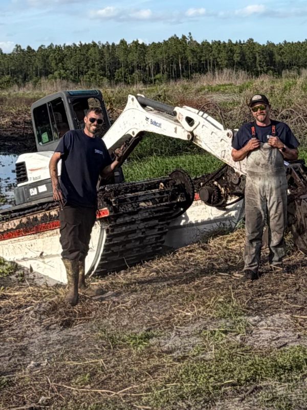 Two men standing beside a large excavator in a field.