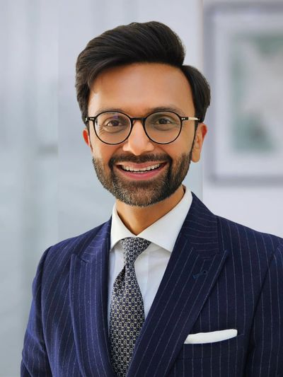 Smiling man in glasses and a pinstripe suit with a patterned tie.