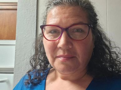 Woman with curly hair and purple glasses smiling.