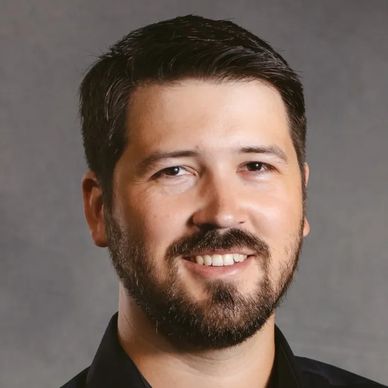 Smiling man with beard and dark hair against a gray background.