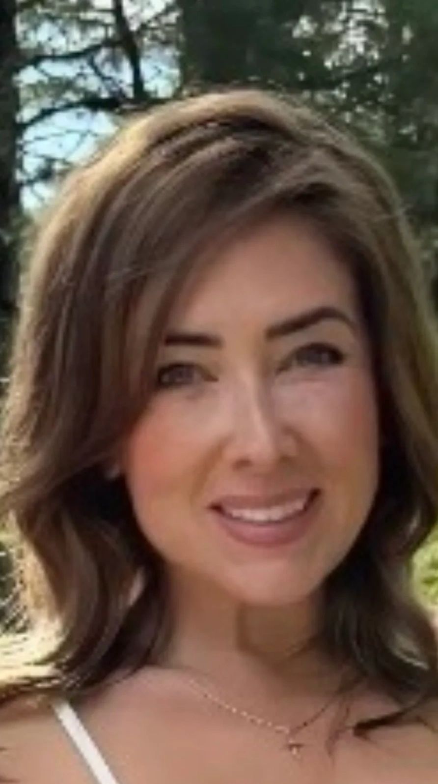 Smiling woman with light brown hair outdoors.