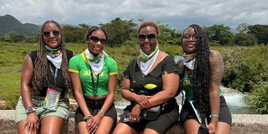 Four women sitting outdoors with greenery and a waterfall behind them.