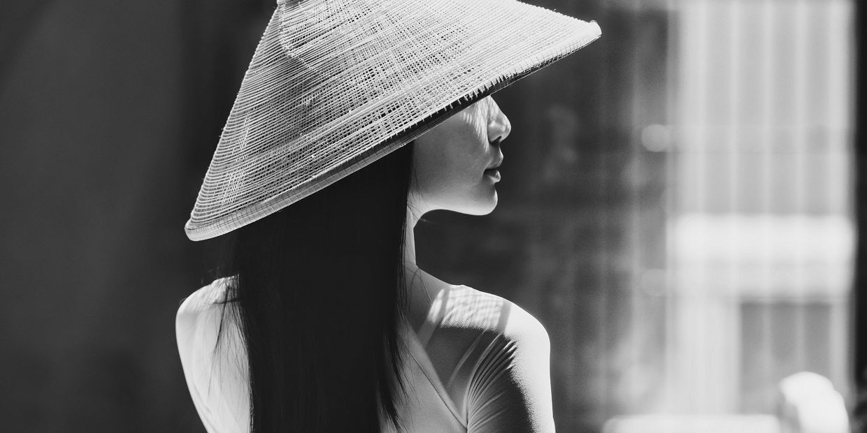 Profile of a woman wearing a traditional conical hat in soft light.