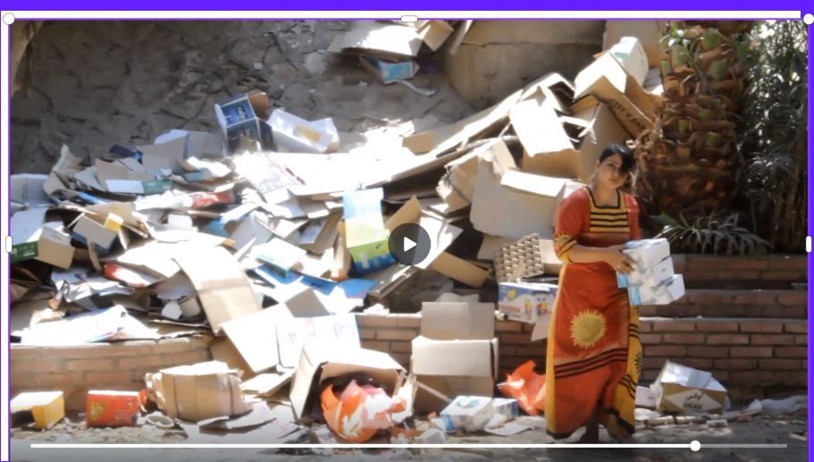 Woman in colorful dress sorting through a large pile of cardboard boxes outdoors.