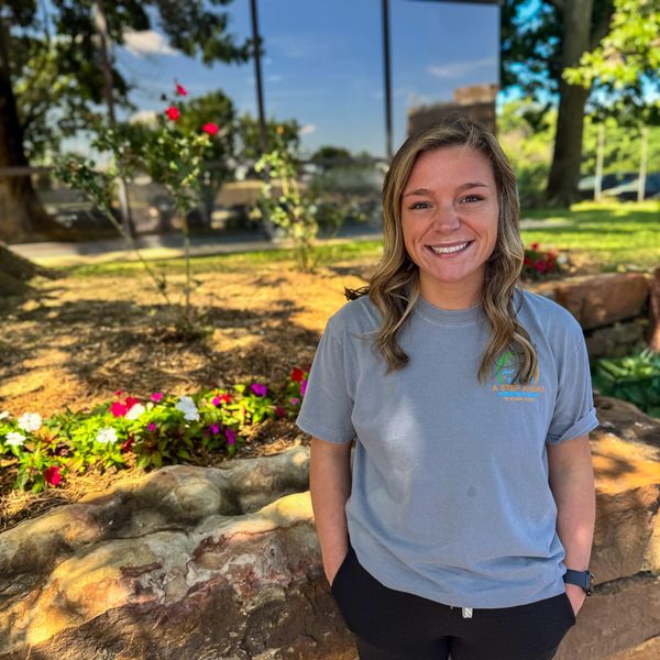Smiling woman standing outdoors near flowers and rocks.