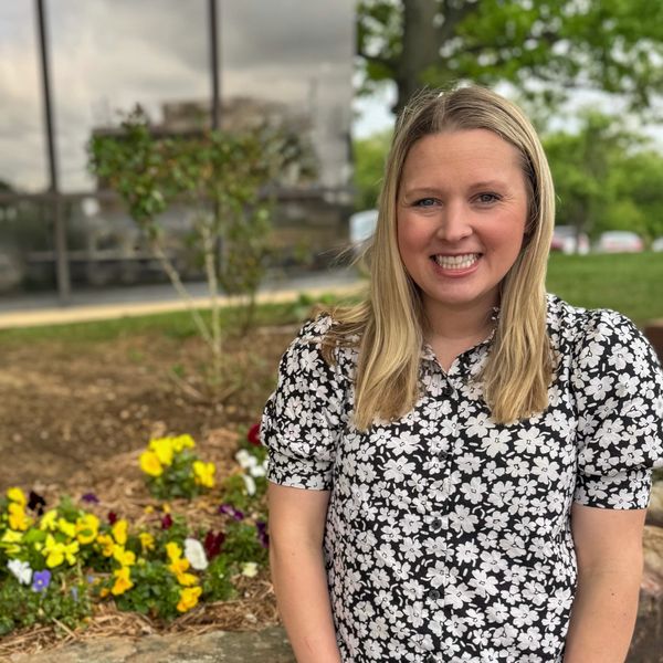 Smiling woman in floral dress near flowers outdoors.