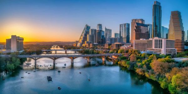 Sunset view of a city skyline with a river and bridges.