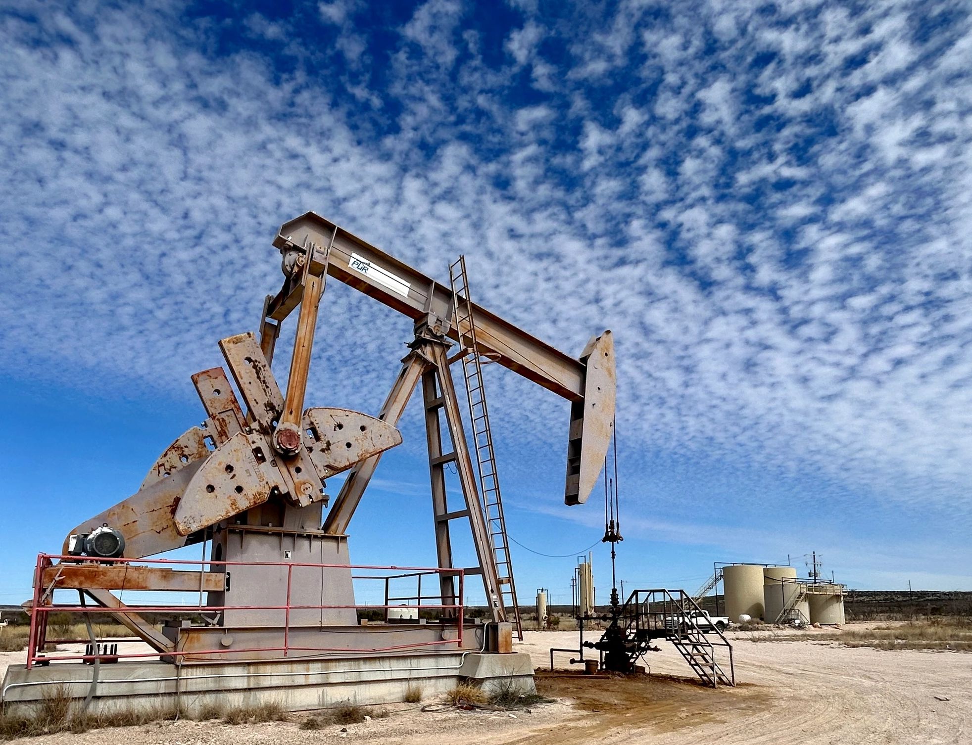 Rusty oil pumpjack under a blue sky with scattered clouds.