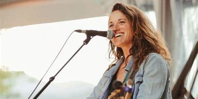 Woman singing and playing guitar on stage with a joyful smile.