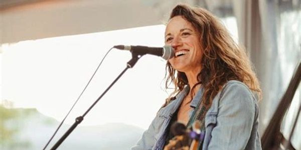 Woman singing and playing guitar on stage with a joyful smile.