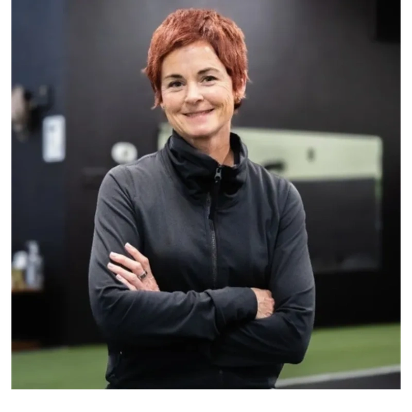 Confident woman with short red hair smiling, arms crossed, wearing a black jacket.