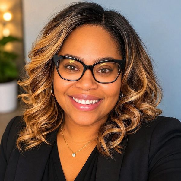 Smiling woman with curly hair and glasses.