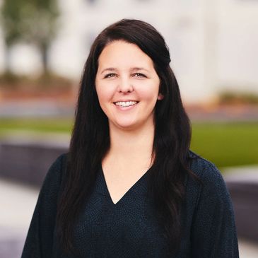 Smiling woman with long dark hair outdoors, dressed in a dark top.