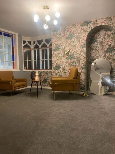 Cozy reception area with mustard chairs, floral wallpaper, and vintage-style lighting.