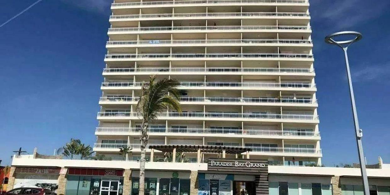 Tall resort building named Paradise Bay Grand under clear blue sky.