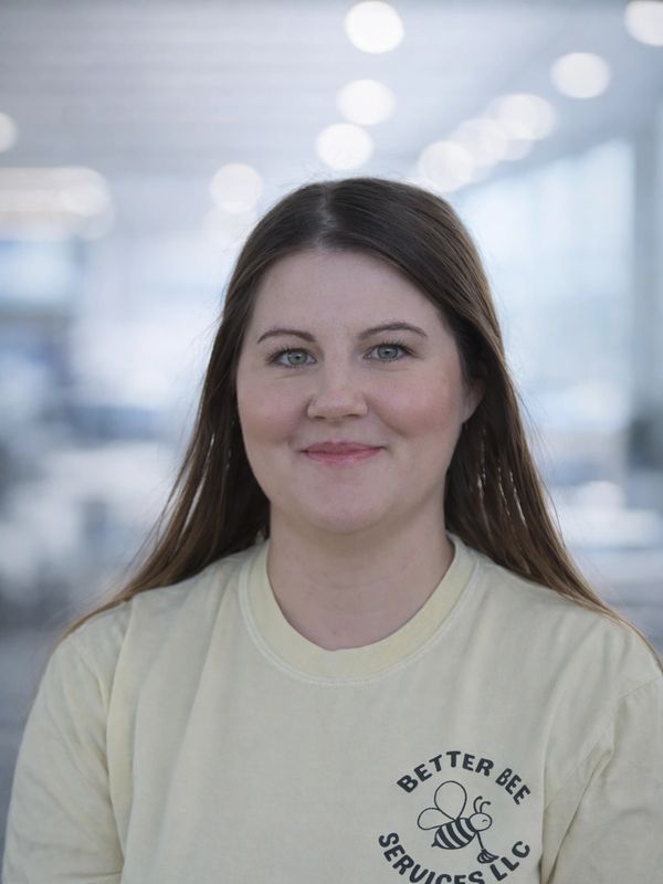 Young woman smiling, wearing a Better Bee Services LLC t-shirt.