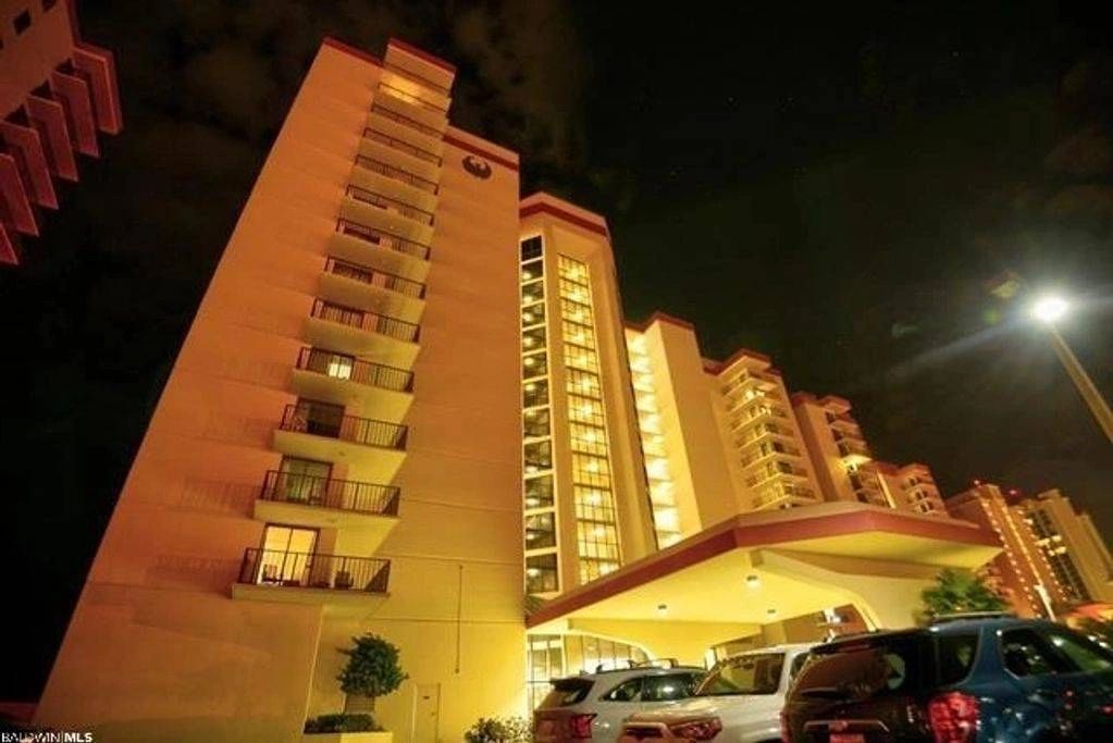 Tall apartment building illuminated at night with parked cars.
