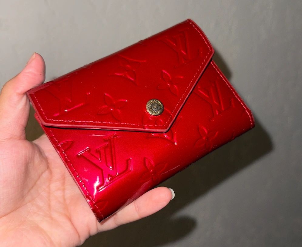 Red Louis Vuitton wallet held in hand.