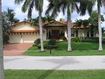 A single-story house with palm trees and a well-maintained lawn.