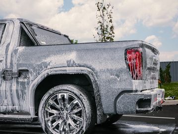 A pickup truck covered in soap foam during a wash outdoors.