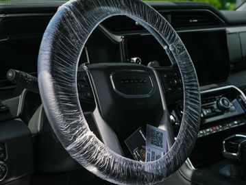 Steering wheel wrapped in protective plastic inside a vehicle.