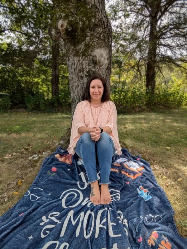 Woman sitting barefoot on a blanket under a tree in a park.