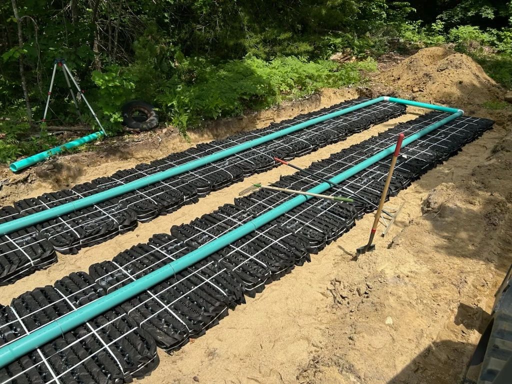Septic site with pipes and black plastic trays laid on sand.
