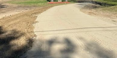 A winding concrete path through a grassy area with shadows.