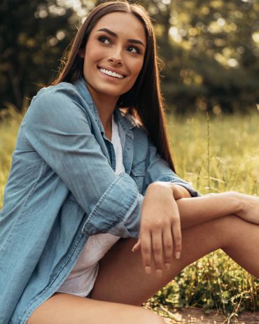 Smiling woman sitting outdoors in a field.
