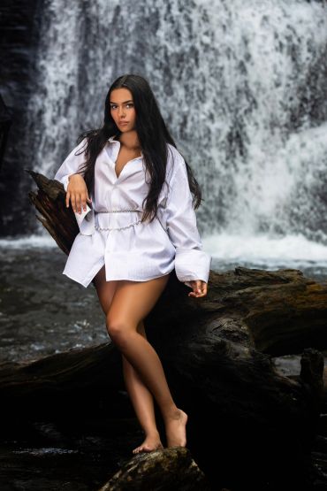 Woman posing by a waterfall in a white shirt.
