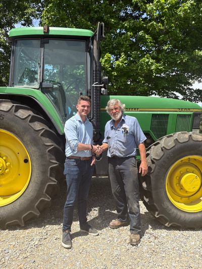 Two men shaking hands in front of a green tractor.