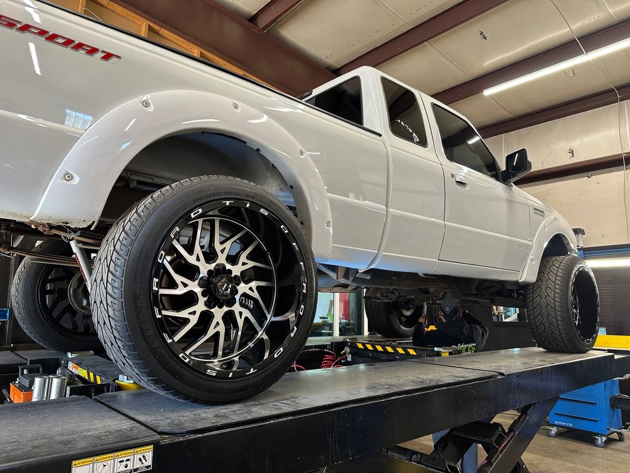 White pickup truck on a lift with black and silver wheels in a garage.