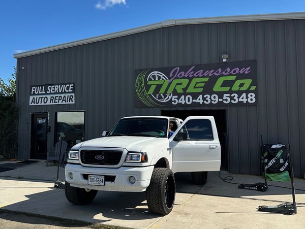 White Ford truck parked outside Johansson Tire Co. auto repair shop.