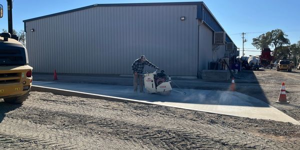 Person cutting concrete outside a building on a sunny day.