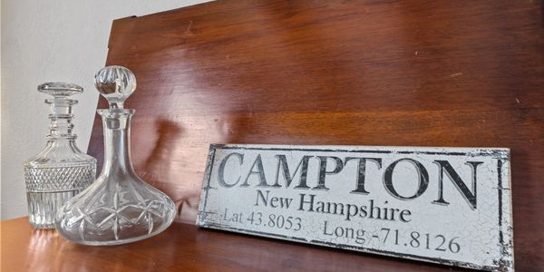 Decorative glass decanters beside a Campton, New Hampshire sign.