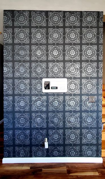 Stenciled pattern with silver metallic paint on a dark grey painted accent wall.