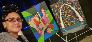 Person smiling with colorful abstract paintings and Gateway Arch artwork.