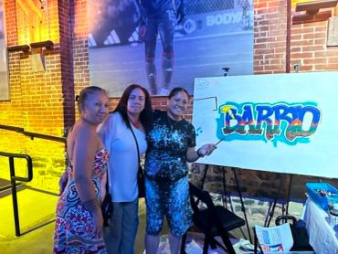 Three women posing with colorful graffiti art.