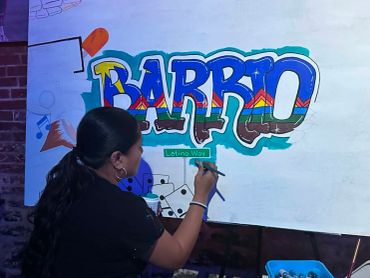 Artist painting colorful 'BARRIO' graffiti.