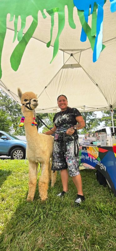 Woman posing with an alpaca at an outdoor event.