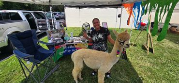 Woman with a friendly alpaca at a community event booth.
