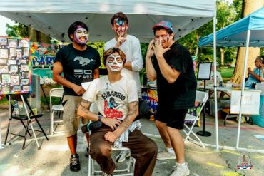 Four men with face paint posing at an outdoor event booth.