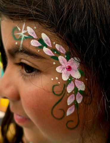 Child with delicate floral face painting in pastel colors.