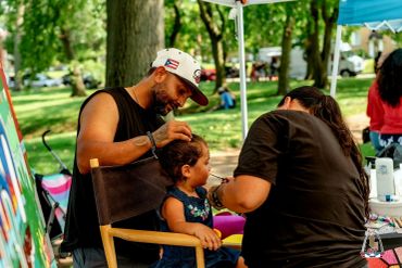 Man styles girl's hair at outdoor event.