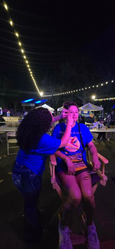 Woman getting face painted under string lights at night event.