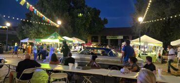 Outdoor night market with people and vintage car.