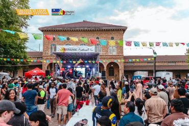 Crowd at a vibrant outdoor festival with stage and flags.