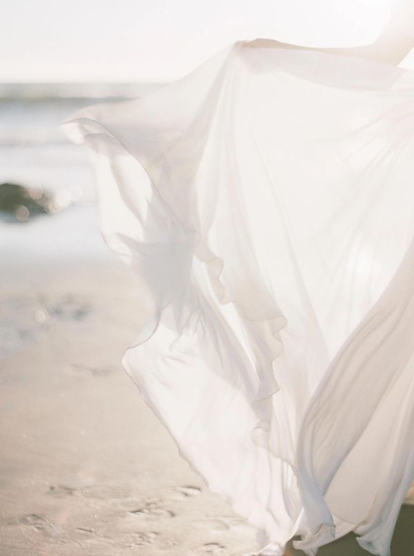 this is an image of a lady on the beach with her dress blowing in the wind.