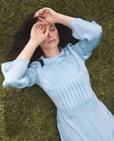 Woman in blue dress lying on grass with eyes closed.
